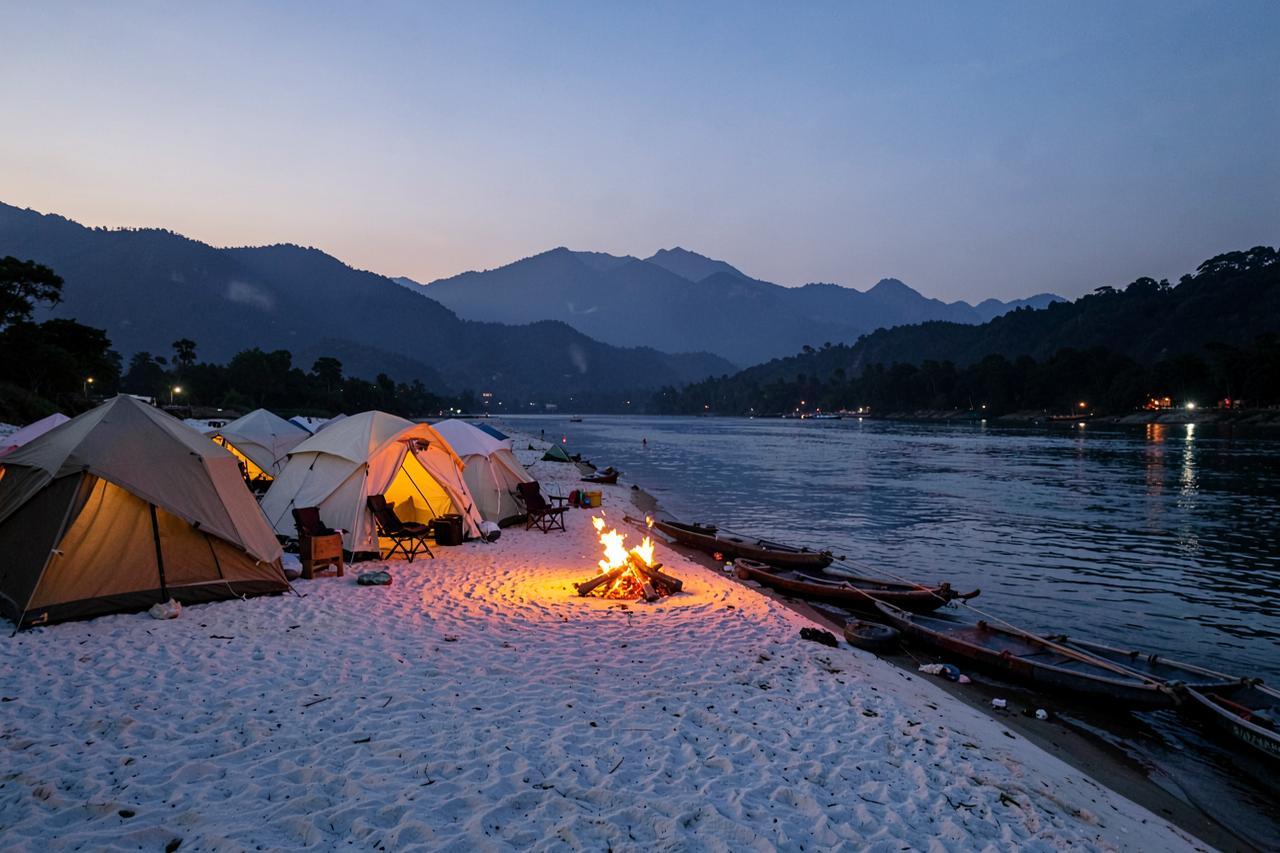 Tents and a campfire on a white sand Ganga beach at dusk during a Devprayag expedition